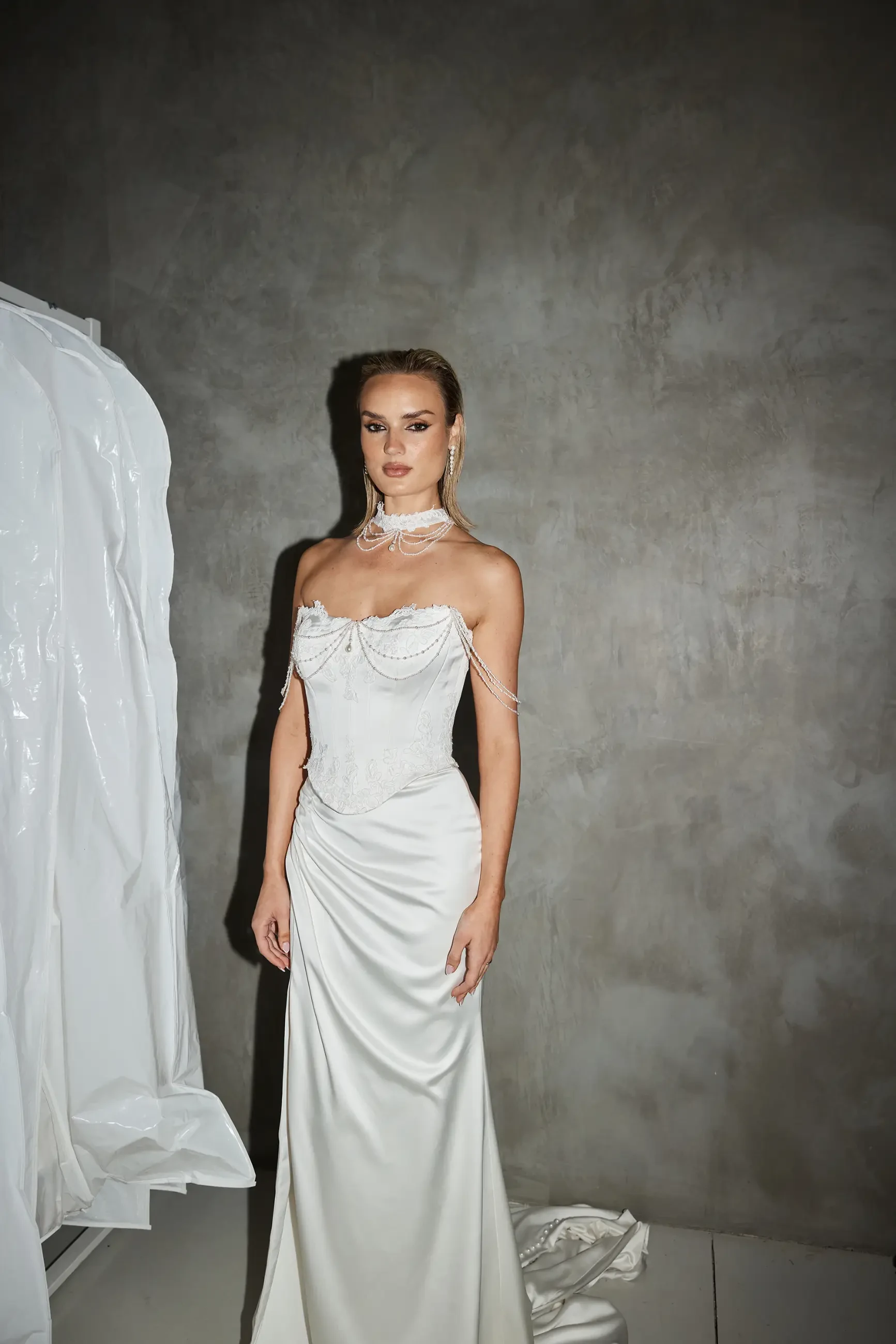 Model is wearing a wedding dress with a structured satin and lace bodice, boned corset, Basque waist, and draped pearl detailing for vintage-inspired elegance.